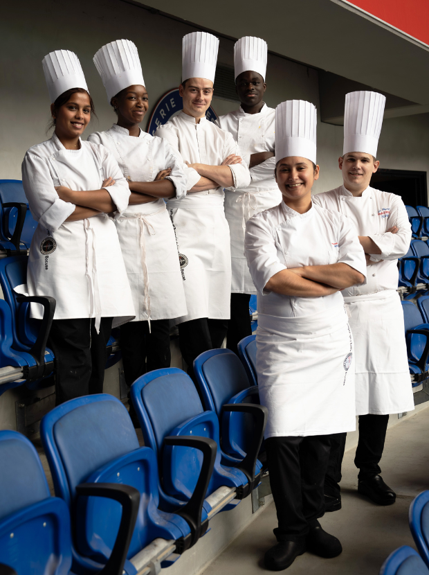 Équipe de cuisiniers en tenue blanche posant dans les gradins du stade Groupama à Lyon.