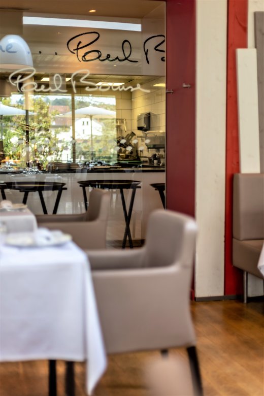Salle du Restaurant Fond Rose à Lyon avec vue sur la cuisine ouverte et la signature de Paul Bocuse.