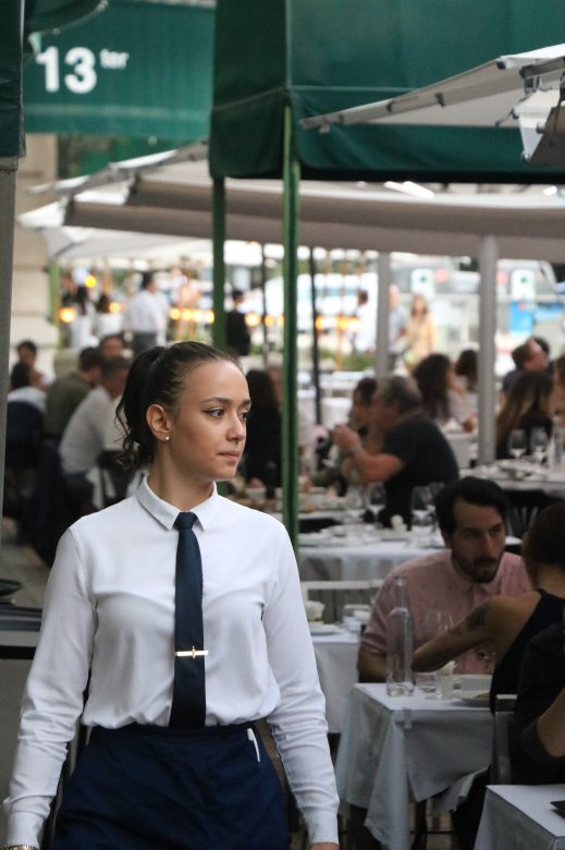 Serveuse en uniforme effectuant le service en terrasse à la Brasserie L’Est, Lyon 6ᵉ, en soirée.