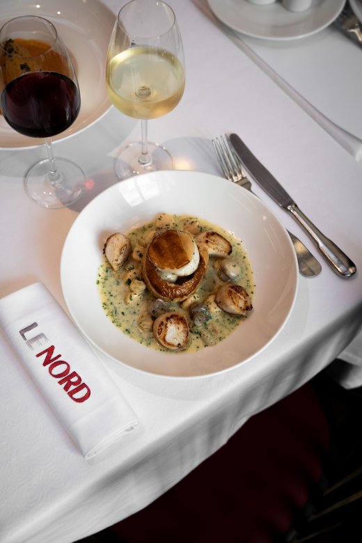 Assiette de coquilles Saint-Jacques et sauce crémeuse, accompagnée de vin blanc à la Brasserie Le Nord.