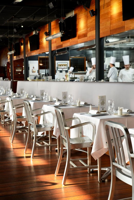 Salle de la Brasserie L'Ouest à Lyon avec cuisine ouverte et chefs en action.